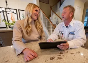 A Dependaworthy Benjamin Franklin Plumbing technician consulting with a homeowner at the kitchen counter in Charlotte, NC.